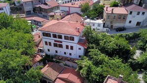 A white building with a red-tiled roof, surrounded by greenery and other buildings. - Anfora Otel & Sarap Evi (Edremit)