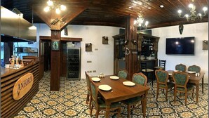 A restaurant with a wooden bar, a dining area with a large table and chairs, a television mounted on the wall, and a patterned floor. - Anfora Otel & Sarap Evi (Edremit)