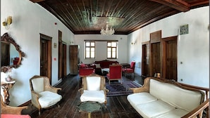 A spacious room with a high ceiling, wooden beams, and a chandelier. There are two sofas, a red armchair, and a small table with a vase. - Anfora Otel & Sarap Evi (Edremit)