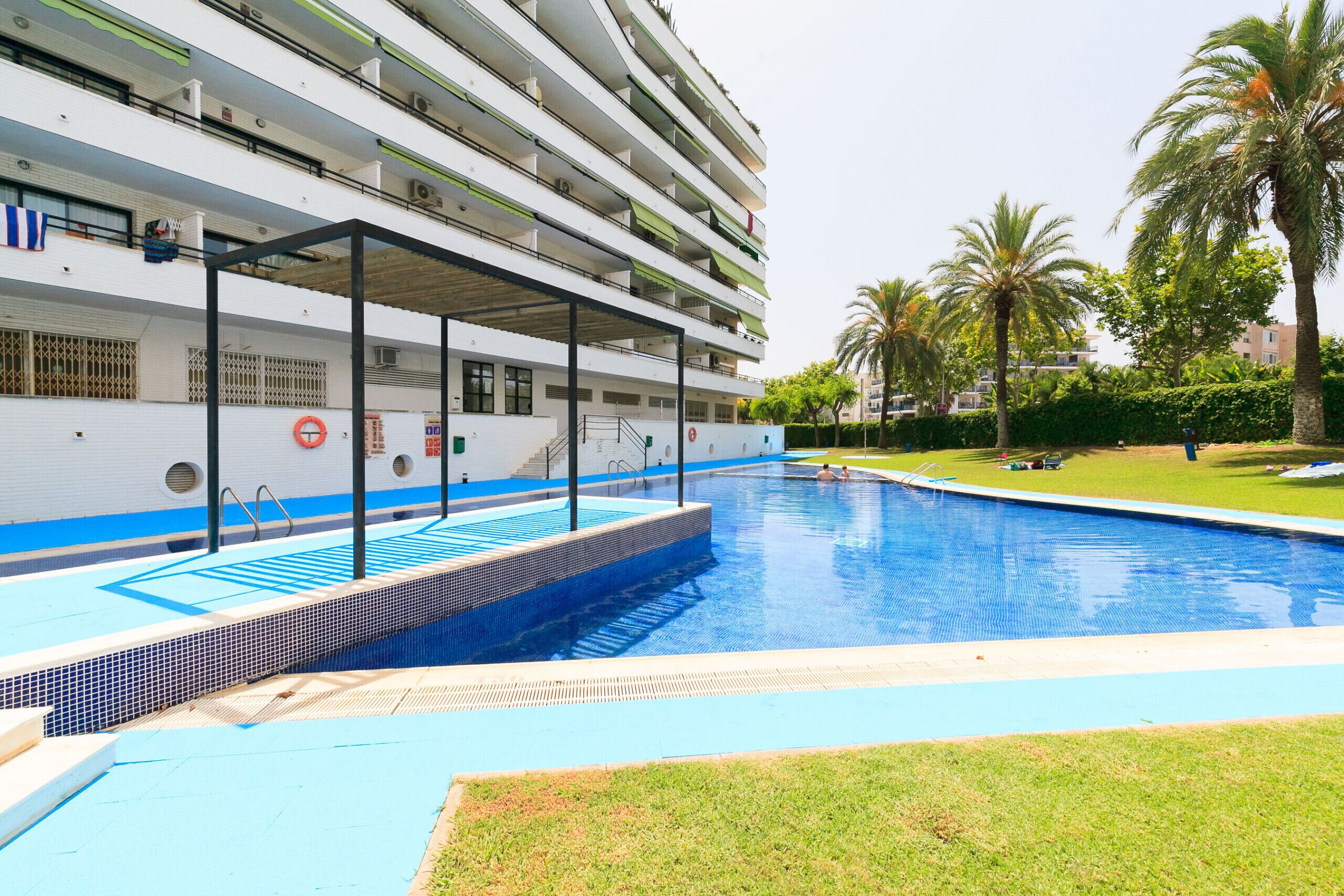 A swimming pool adjacent to a multi-story building with balconies.