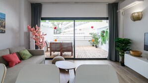 Een moderne woonkamer met een bank, een bijzettafeltje en een balkon met uitzicht op een gebouw en beplanting.