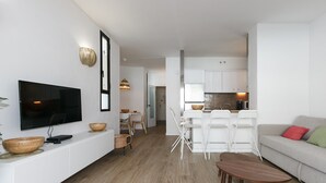 Een moderne woonkamer met een flatscreen televisie, houten kommen, een eethoek met stoelen, en een keuken met witte kasten.