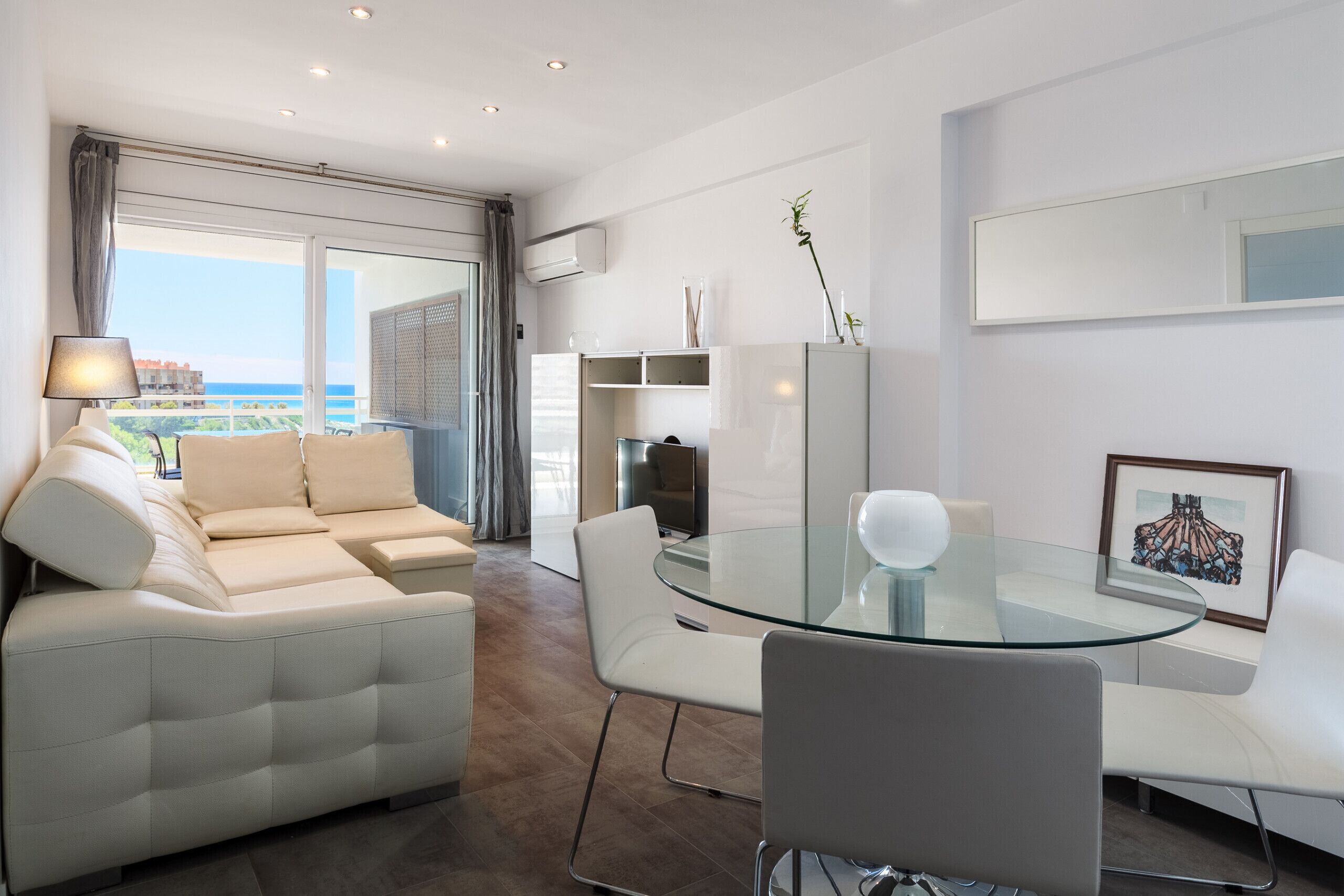 Una sala de estar moderna con una mesa de comedor de cristal, sofás blancos y vista al mar.
