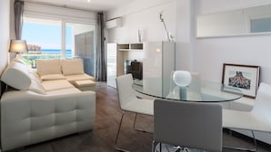 A modern living room with a glass-top dining table, white sofas, and a view of the sea. - AirCon Apartment · Beachfront · WiFi · UHC SCALA MAR 305 (Salou)