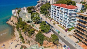 A coastal cityscape with a prominent multi-story hotel featuring balconies, a beach, and a clear view of the sea. - AirCon Apartment · Beachfront · WiFi · UHC SCALA MAR 305 (Salou)