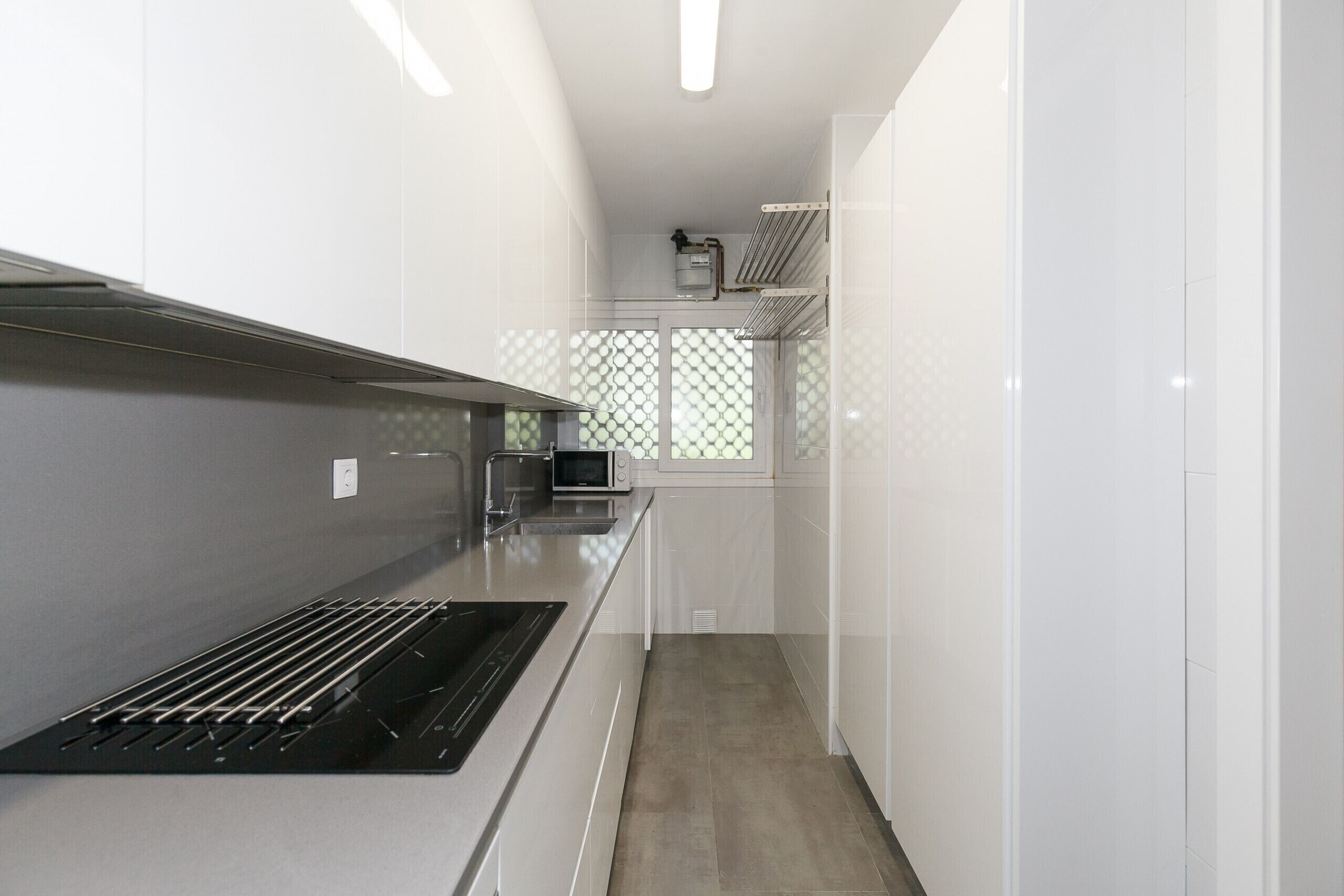 Una cocina moderna con armarios blancos, una campana extractora de acero inoxidable y un microondas.