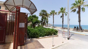 Un bâtiment situé en bord de mer, doté d’une entrée couverte, de palmiers et offrant une vue dégagée sur l’océan.