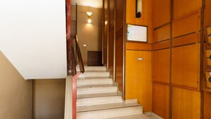 Un escalier avec des panneaux de bois et une main courante, menant à un palier où se trouve une pancarte.