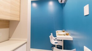 A small room with a blue wall, a white table with a chair, and a white air conditioning unit. - GuestHost - Clouds Apartment x3 5 meters from the beach! (Trani)