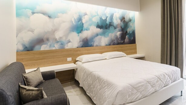 A modern bedroom with a large bed, a sofa, and a wall-mounted artwork. - GuestHost - Clouds Apartment x3 5 meters from the beach! (Trani)