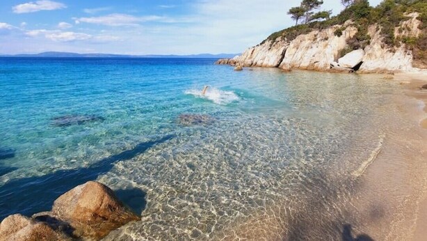 Une plage dégagée, avec une eau peu profonde, des rochers et une côte visible au loin.