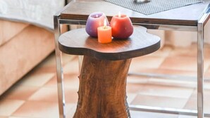 Une table en bois avec un pied original en forme de tronc d’arbre, un verre d’eau et trois bougies disposées sur un plateau.