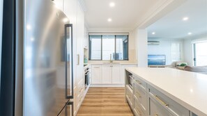 A modern kitchen with white cabinetry, a stainless steel refrigerator, and a wooden floor.