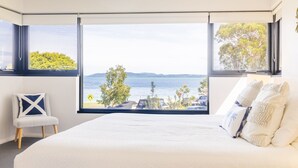 Un dormitorio con una cama grande, una silla y vistas a un lago y árboles.