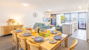 Un comedor moderno con una mesa de madera dispuesta para una comida, un sofá y una cocina al fondo.