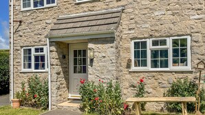 Une maison en pierre avec une porte d’entrée, deux fenêtres au rez-de-chaussée et un banc dans le jardin.