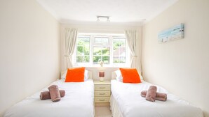 Une chambre d’hôtel avec deux lits, une fenêtre avec des rideaux, une table de chevet avec une lampe et un tableau au mur.