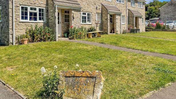 Une maison en pierre avec un porche à l’avant, une pelouse et une enseigne indiquant « Chestnut Court ».