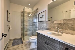 A modern bathroom with a glass shower enclosure, a white toilet, a large sink with a marble countertop, and a dark wooden vanity. - Grand Lake Condo w/ Balcony & Mountain Views (Grand Lake)