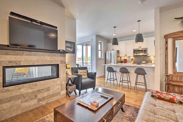 A modern living room with a fireplace, a flat-screen TV mounted above it, and a cozy seating area with a sofa and a coffee table. - Grand Lake Condo w/ Balcony & Mountain Views (Grand Lake)