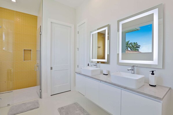 Un baño moderno con dos lavamanos, una ducha y una puerta que da a otra habitación.
