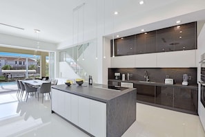 A modern kitchen with a central island, built-in appliances, and a glass staircase. - Villa Juhara - Welcome to Paradies (Cape Coral)