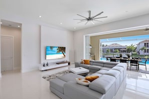 A modern living room with a large gray sectional sofa, a flat-screen TV mounted on the wall, and a ceiling fan.