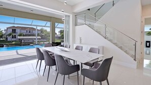 Un comedor moderno con vista a la piscina, una escalera de cristal y un ventanal grande.