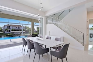 A modern dining area with a pool view, a glass staircase, and a large window.