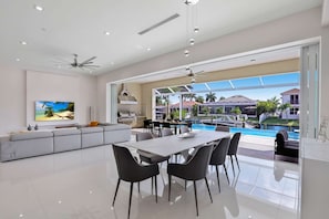A modern kitchen with a gas stove, a dining area with a white table and chairs, and a large window overlooking a pool and resort. - Villa Juhara - Welcome to Paradies (Cape Coral)