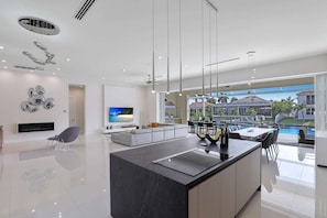 A modern kitchen with a central island, a dining area with a pool view, and a living room with a TV.