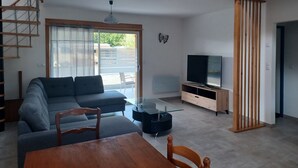 A modern living room with a sofa, a dining table, and a TV. - Gîtes les 2 Clos au Pied du Mont (Pontorson)