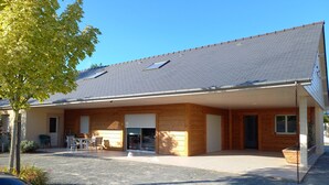 A two-story building with a sloped roof, a covered patio area, and a car parked in front. - Gîtes les 2 Clos au Pied du Mont (Pontorson)