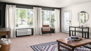 A modern living room with large windows, a brown leather sofa, a wooden coffee table, and a round mirror on the wall. - Lovely Pet Friendly 2bd / 2ba w/ Private Entrance, On Site Laundry & Dedicated Parking (Paradise)