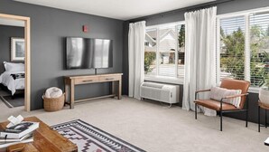 A modern living room with a grey wall, a wooden desk, a TV, a window with curtains, a brown leather chair, and a patterned rug. - Lovely Pet Friendly 2bd / 2ba w/ Private Entrance, On Site Laundry & Dedicated Parking (Paradise)
