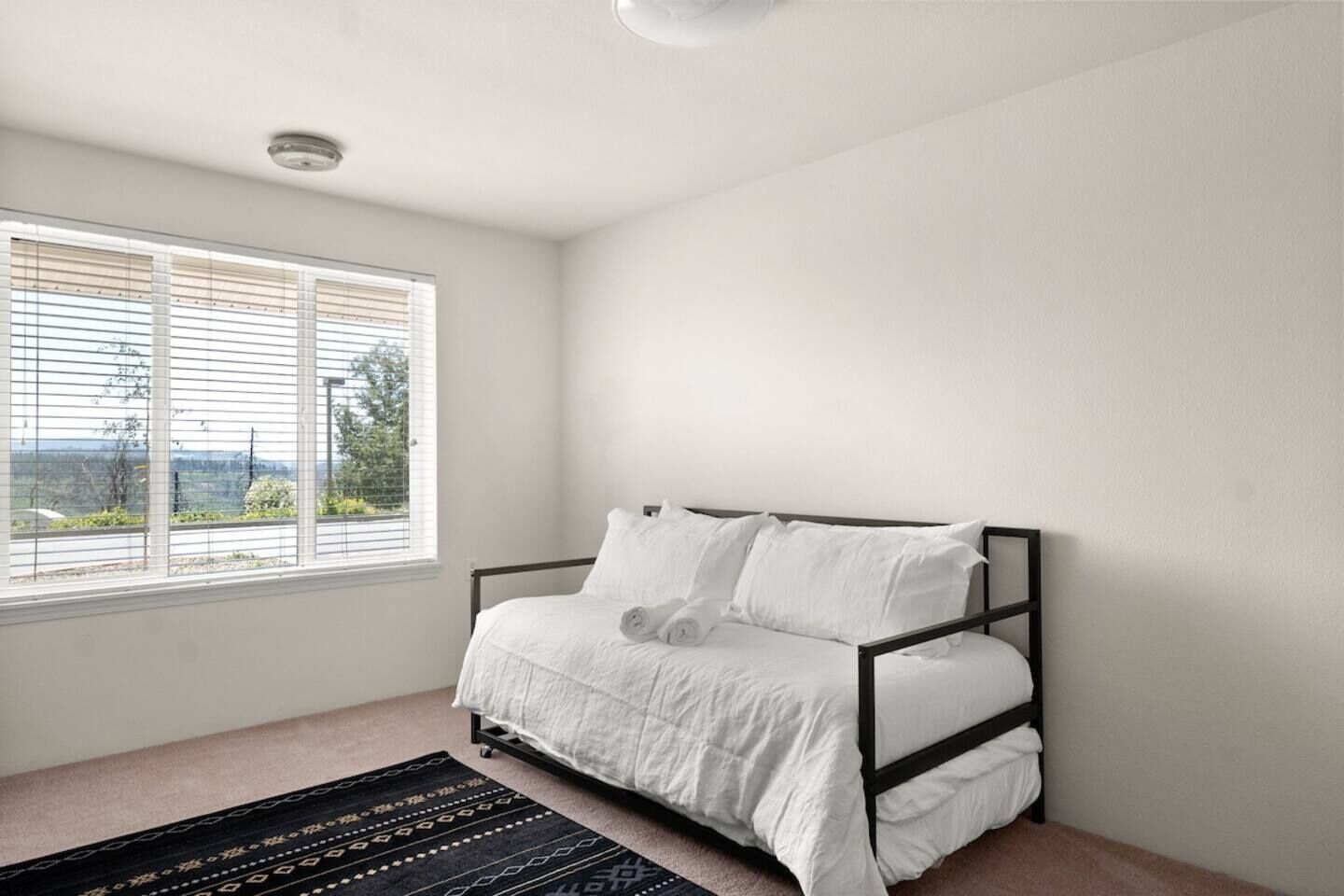 A bedroom with a bed, a window with blinds, and a ceiling light.