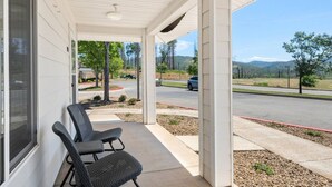 A covered porch with two chairs, a view of a road, and a distant landscape. - Lovely Pet Friendly 2bd / 2ba w/ Private Entrance, On Site Laundry & Dedicated Parking (Paradise)