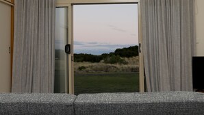 A hotel room with a large bed, a view of the outdoors through a sliding glass door, and a ceiling light fixture. - Stanley Beach House with Stunning Views of the Nut! (Stanley)