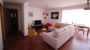 A living room with a sofa, a TV, a red bean bag, and a dining area with a table and chairs. - Ideal apartment for large families and groups of friends (Corralejo)
