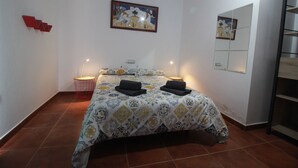 A bedroom with a patterned bedspread, a bedside table with a lamp, and a wall-mounted mirror. - Ideal apartment for large families and groups of friends (Corralejo)