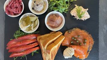 A variety of food items including smoked salmon, pickles, and bread on a slate board.