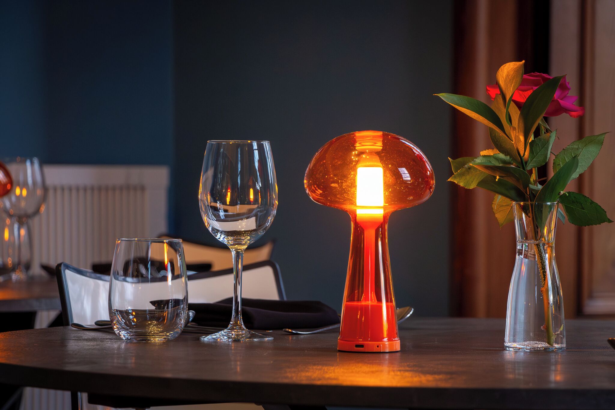 Una mesa con dos vasos, una lámpara encendida y un florero con flores.