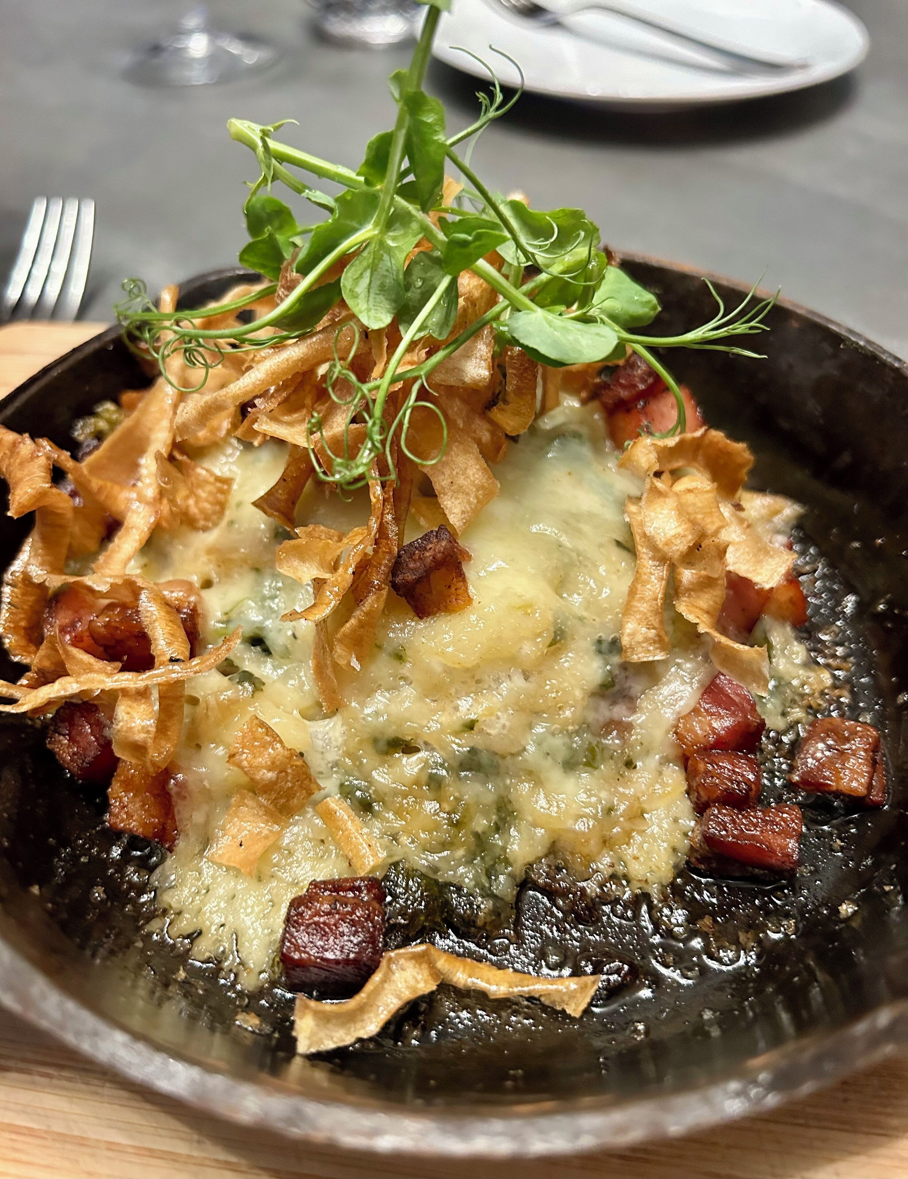 A dish with crispy bacon, cheese, and greens on a plate.