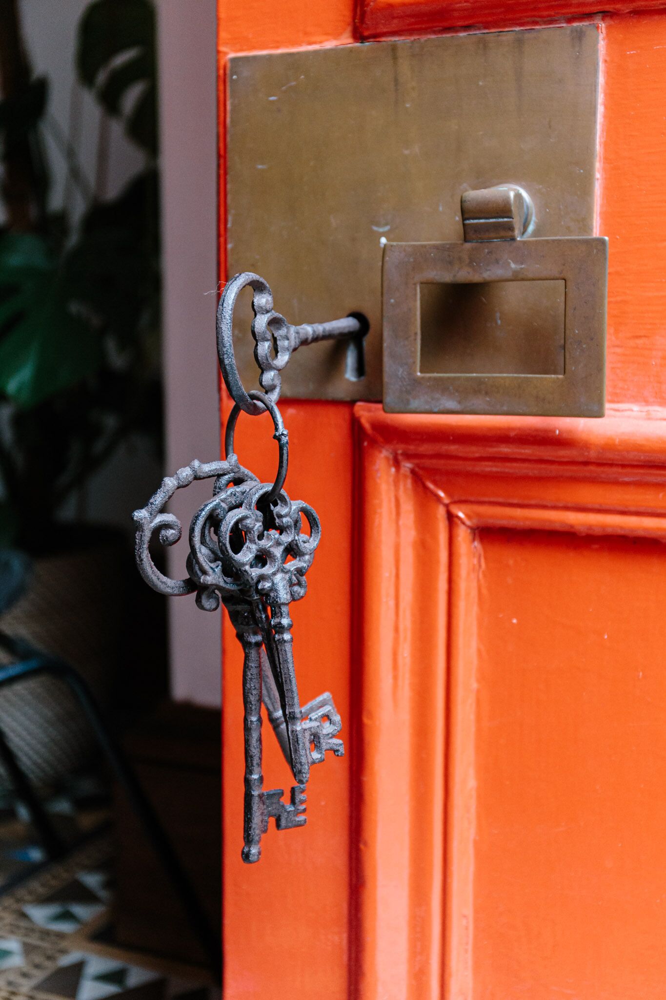 Une serrure en laiton avec un trou de serrure et une clé insérée, fixée à une porte orange ornée d’une plaque en laiton et d’une petite boîte rectangulaire placée au-dessus.