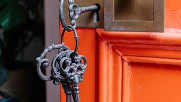 Une serrure en laiton avec un trou de serrure et une clé insérée, fixée à une porte orange ornée d’une plaque en laiton et d’une petite boîte rectangulaire placée au-dessus.