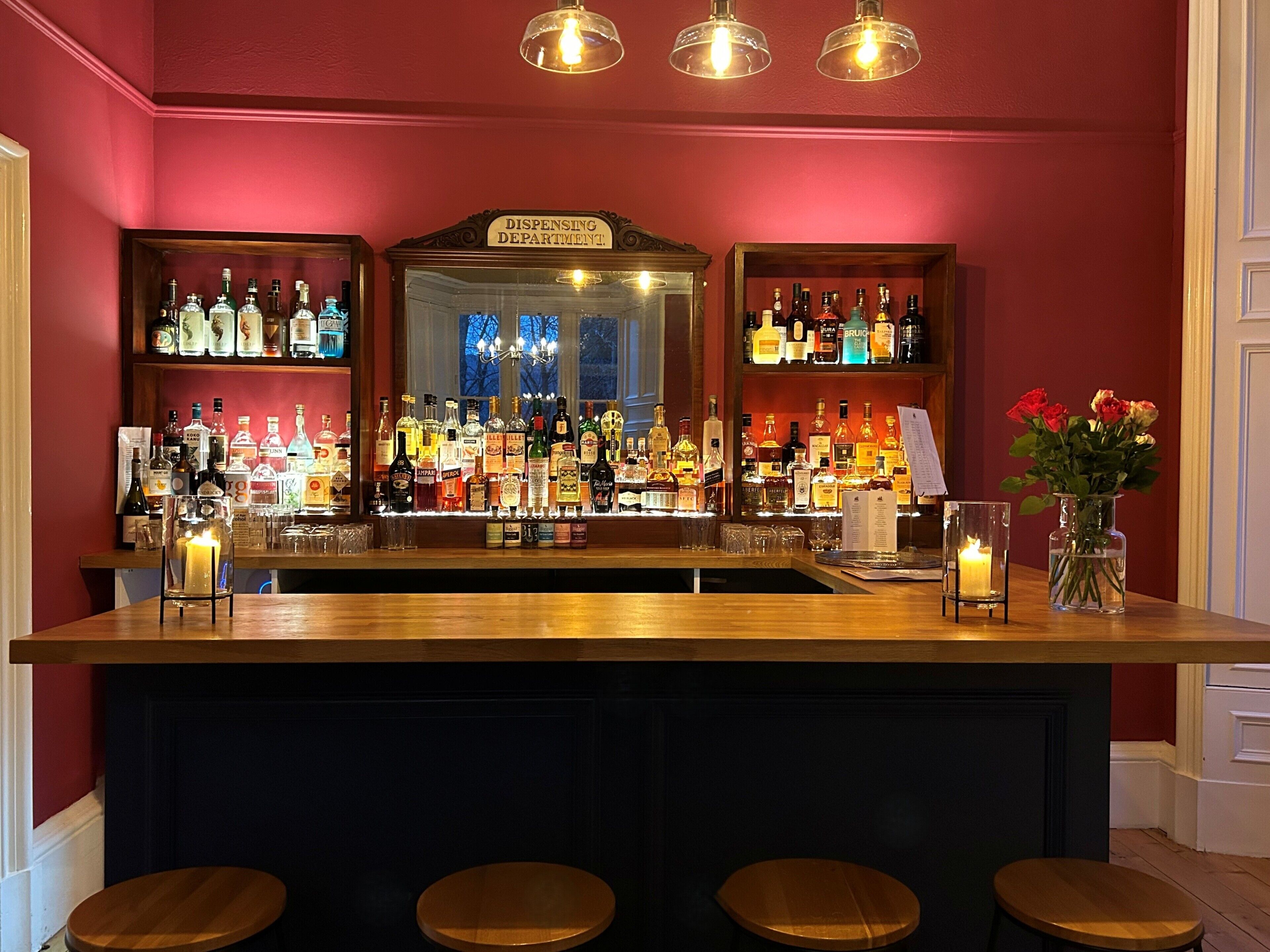 A bar area with shelves of liquor bottles, a sign reading "DISPENSING DEPARTMENT," and a vase with flowers on the counter.