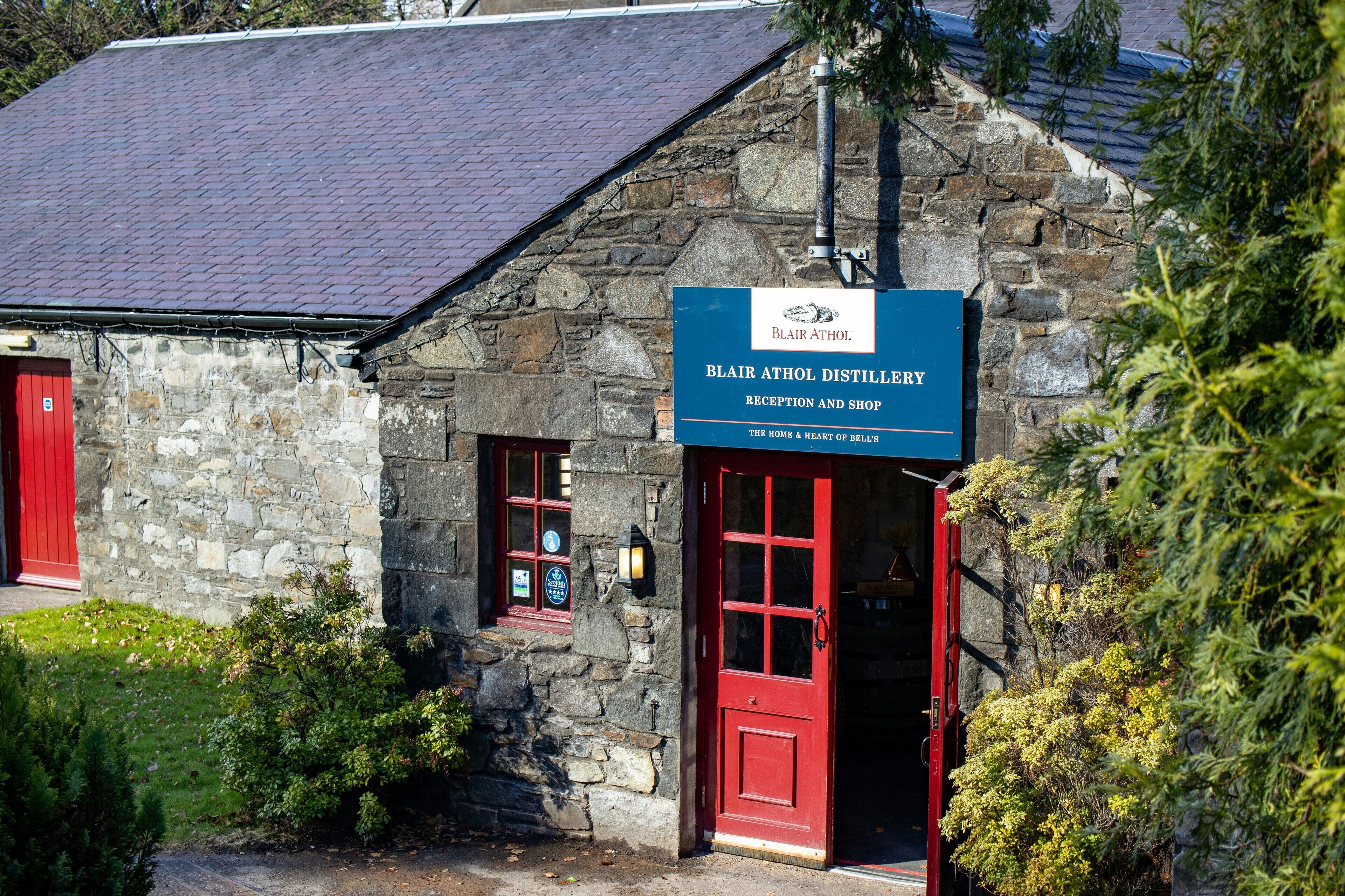 A stone building with a red door and a sign for Blair Athol Distillery.