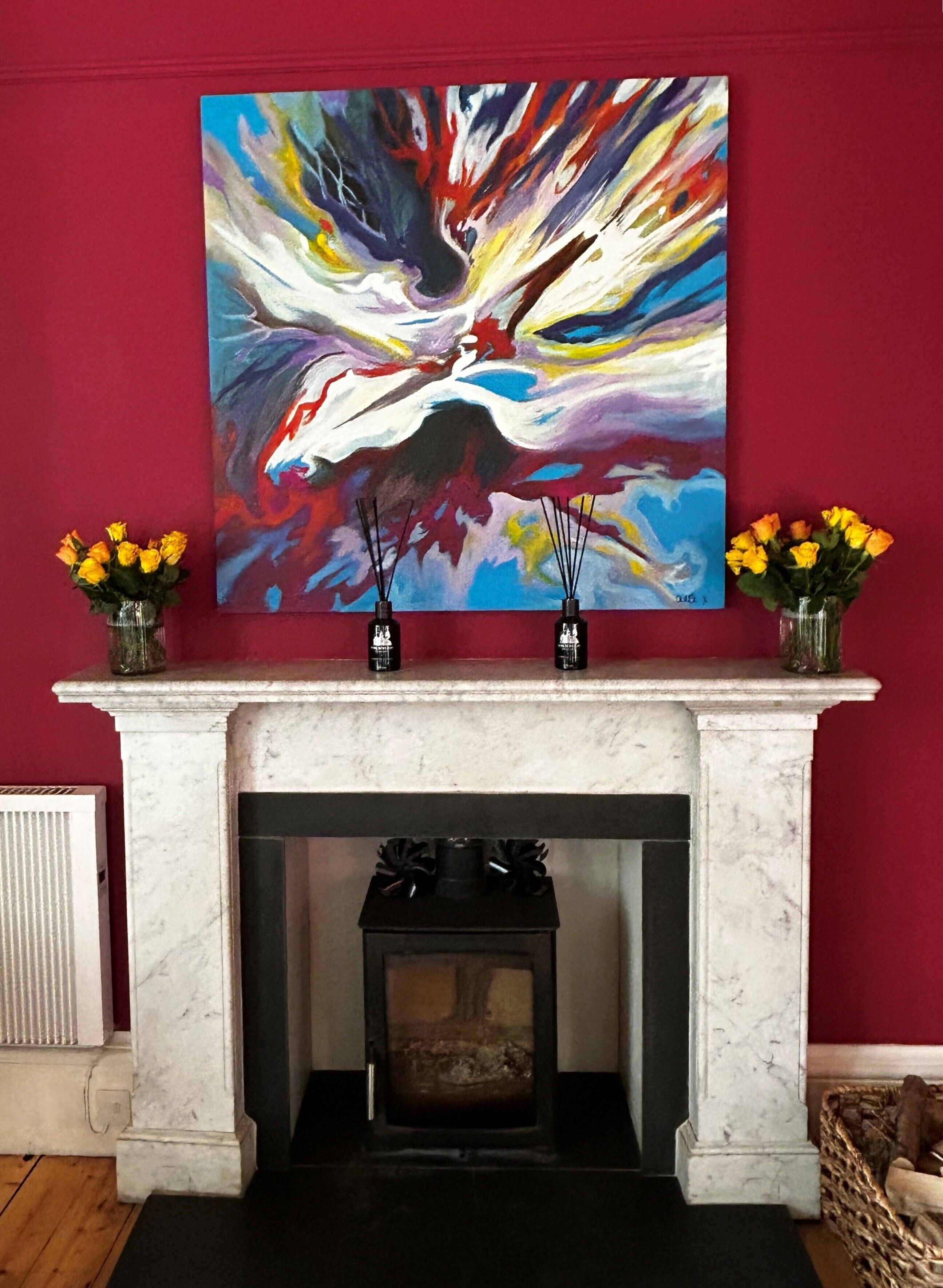 A fireplace with a marble mantel, two vases with yellow flowers, and a colorful abstract painting on the wall.