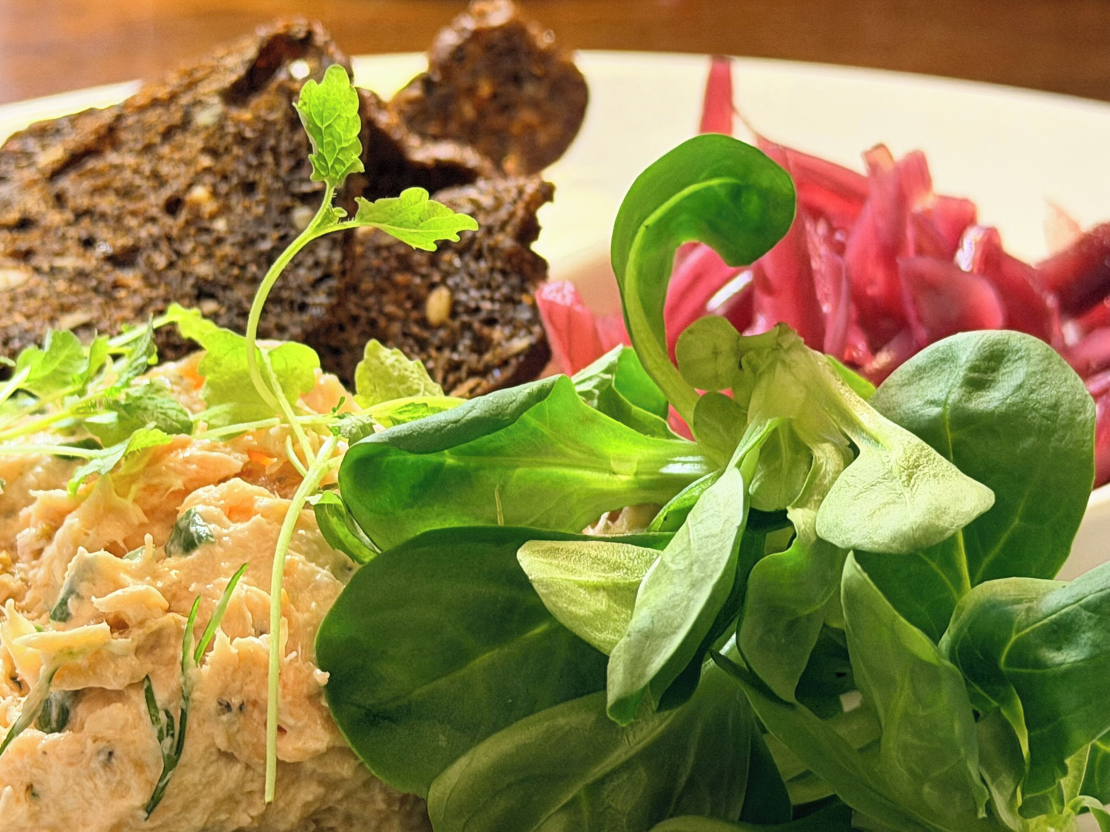 A plate with a variety of food items including greens, a creamy spread, and dark bread.