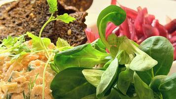 A plate with a variety of food items including greens, a creamy spread, and dark bread.